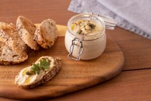 A bowl of creamy old-fashioned pimento cheese spread garnished with fresh parsley, served with crackers and fresh vegetables.